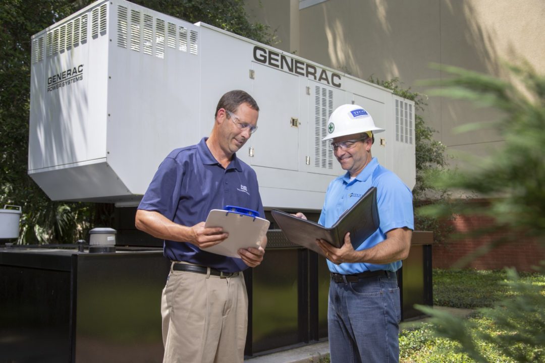 Two people standing in front of a Standby Generator.